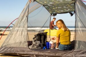 A couple enjoying beach camping with a view of the sea from their tent.