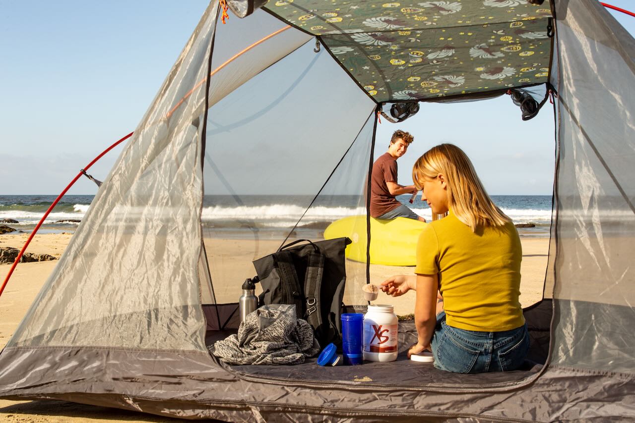 A couple enjoying beach camping with a view of the sea from their tent.