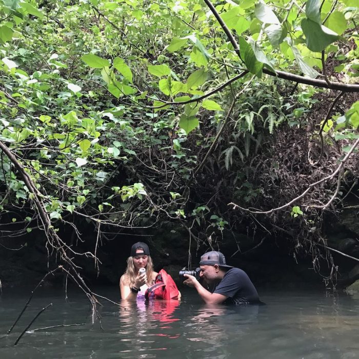 man shooting with actor in waist high water with jungle type environment in the background