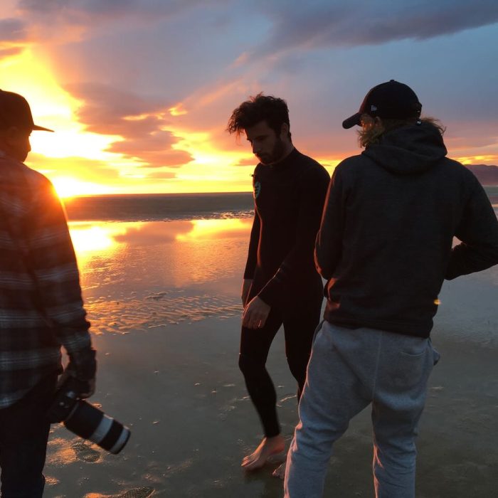 two men on a beach during sunset getting ready to shoot with talent wearing a wetsuit.
