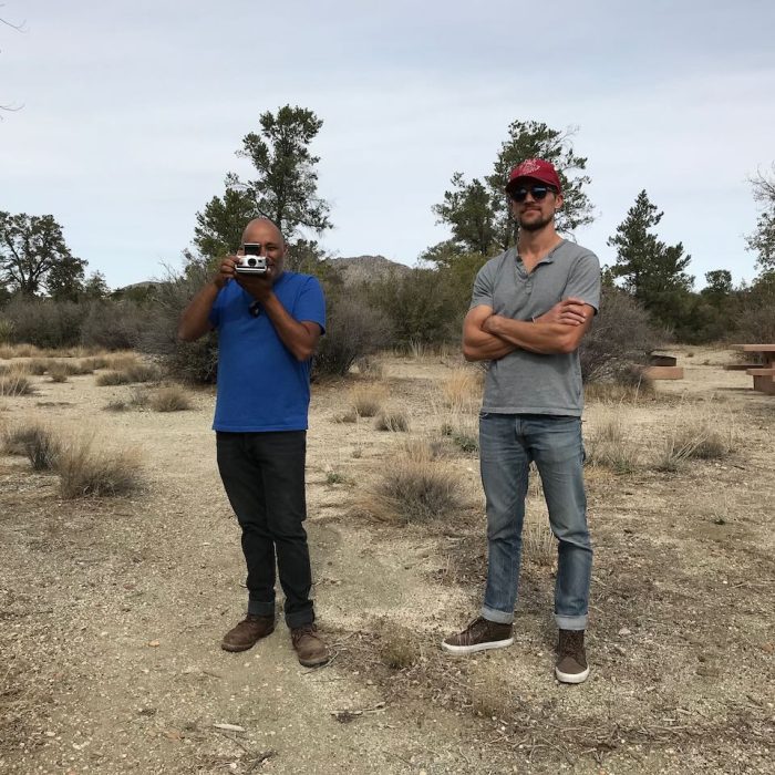 two men standing taking a Polaroid picture at the camera