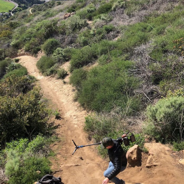 Behind the scenes of shoot with camera operator climbing down hills and rocks
