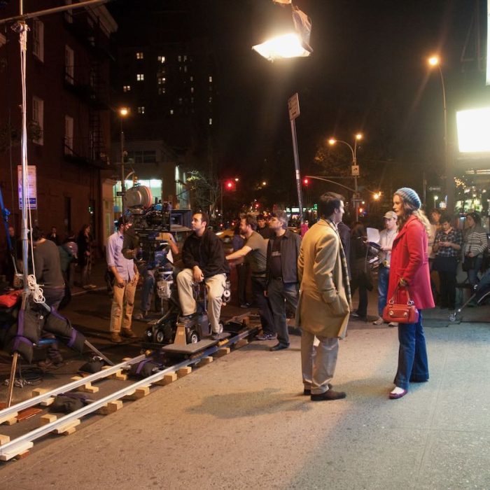 Behind the scenes on a movie shoot with various actors and crew in the background