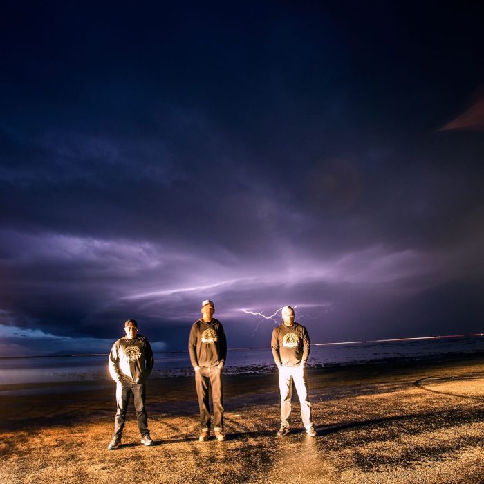 Three men facing the camera with lightning flashing in background